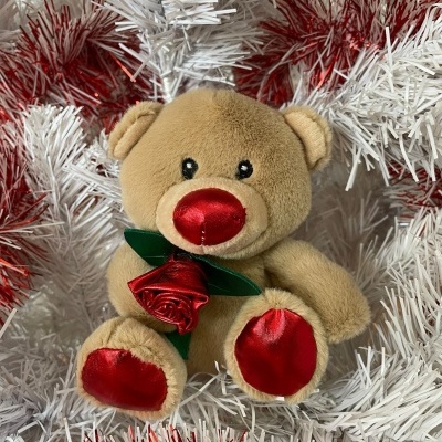 Ursinho de peluche castanho com detalhes vermelhos segurando uma rosa entre decoração natalícia branca e vermelha