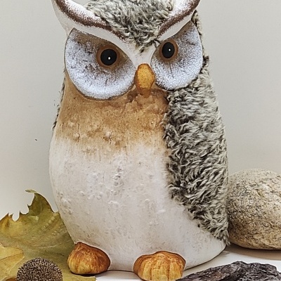 Figura decorativa de coruja marrom e branca com olhos castanhos e bico alaranjado em cenário natural