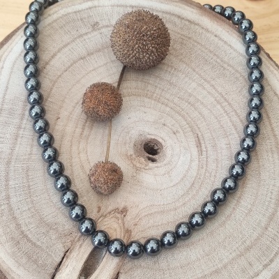 Colar de esferas metálicas prateadas sobre tronco de madeira com frutos secos marrons