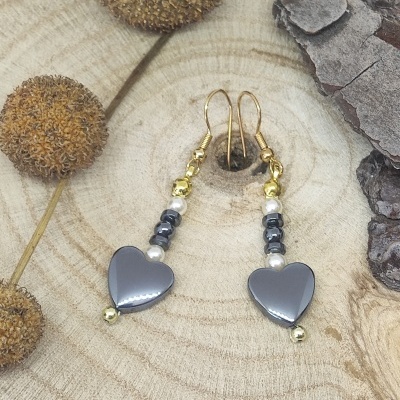 Brincos pendentes com corações cinza e contas douradas sobre madeira