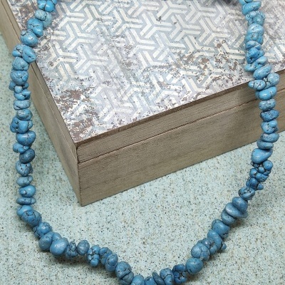 Colar de contas azuis irregulares sobre caixa de madeira com tampa decorada
