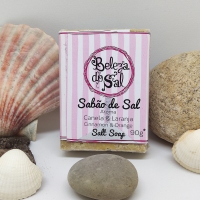 Sabão de sal embalado com rótulo rosa e branco listado entre pedras e conchas