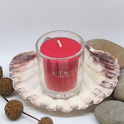 Vela vermelha em copo de vidro com texto HEART & HOME, numa concha decorativa com pedras e elementos naturais