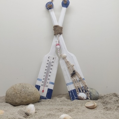 Dois remos decorativos brancos e azuis com termómetro e rede com conchas em ambiente de areia com pedras