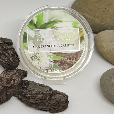 Vela perfumada Chá Branco e Eucalipto em embalagem transparente com etiqueta decorativa, rodeada por casca de árvore e pedras