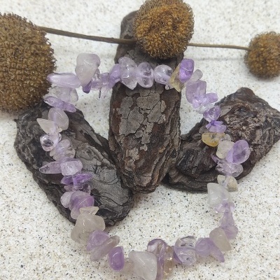 Pulseira de pedras lilás e transparente sobre madeira escura e fundo claro.