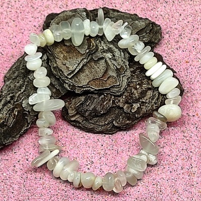 Pulseira elástica de pedras translúcidas claras sobre casca de árvore e fundo rosa granuloso