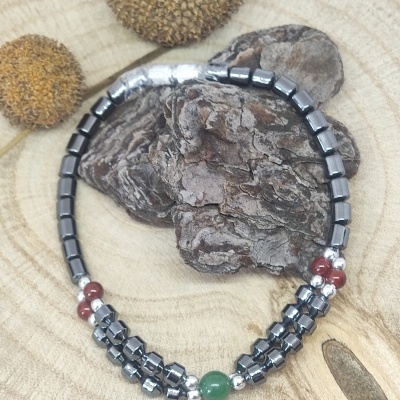 Pulseira com contas metálicas sobre casca de árvore e madeira com sementes