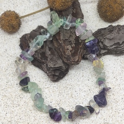 Pulseira de pedras coloridas irregulares sobre fundo claro com casca de árvore e flores secas