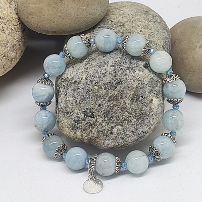 Pulseira azul clara com espaçadores metálicos prateados e pendente, sobre pedras naturais.