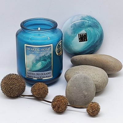 Vela aromática azul com etiqueta e pedras cinzentas ao lado