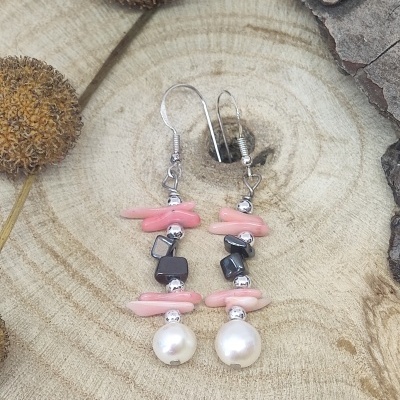 Brincos pendentes com pedras cor-de-rosa, contas prateadas, pedras pretas e pérolas sobre superfície de madeira