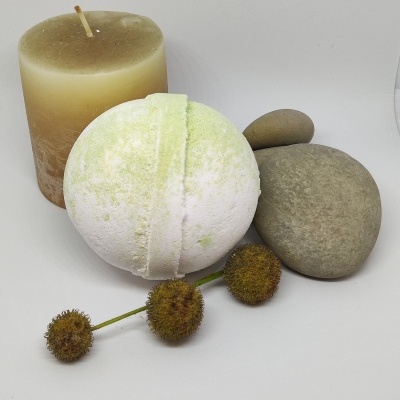 Vela bege, bola efervescente branca com verde, seixos cinzentos e ramo com frutos secos sobre fundo branco.