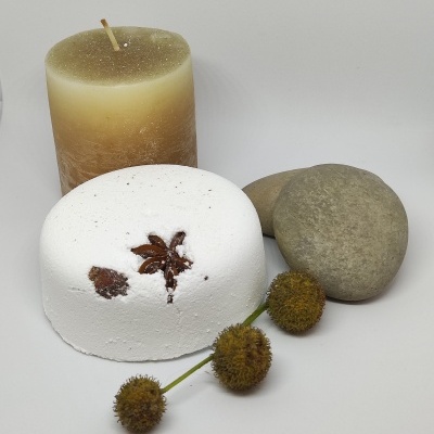 Vela marrom, bloco branco com especiarias, dois seixos e frutos secos sobre fundo branco