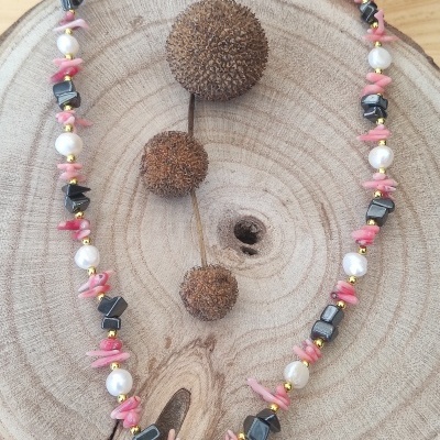 Colar com pérolas brancas, pedras pretas e fragmentos cor-de-rosa sobre madeira redonda com frutos secos