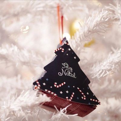 Ornamento de árvore de Natal preto com texto 'Feliz Natal' pendurado numa árvore branca