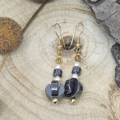 Brincos pendentes com contas amarelas, pérolas brancas e peças cinzentas metálicas sobre madeira