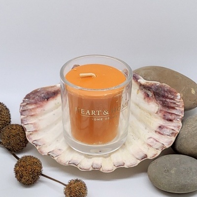 vela laranja em copo de vidro sobre concha rodeada por pedras e frutos secos