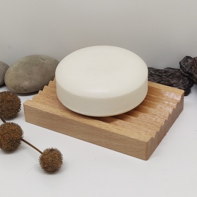 Sabonete branco redondo numa base de madeira com pedras e flores secas à volta