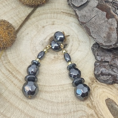 Brincos pretos facetados com detalhes dourados numa superfície de madeira rústica