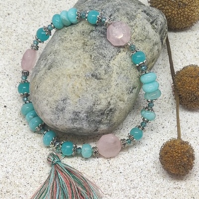 Pulseira de contas azuis e rosas com pendente de fio sobre pedra cinzenta em fundo de areia clara