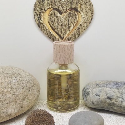 Frasco de vidro com tampa de madeira rodeado por pedras e decoração em forma de coração de madeira.