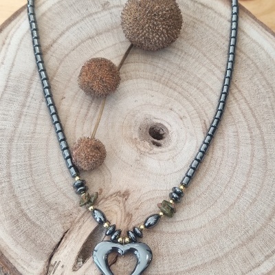 Colar com contas metálicas e pingente em forma de coração sobre base de madeira