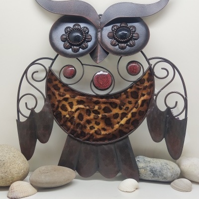 Escultura decorativa de coruja em metal com padrão de pelo e olhos decorados sobre superfície com pedras e conchas