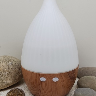 Difusor com base em madeira clara e parte superior branca texturizada em ambiente com pedras decorativas