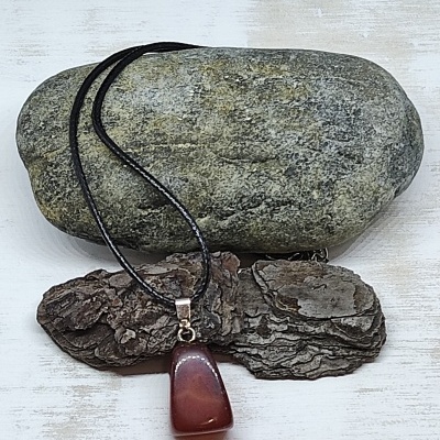 Colar com pendente em pedra polida castanha e cordão preto sobre pedra e casca de árvore