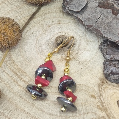 Brincos dourados, pretos e vermelhos sobre madeira clara com textura natural