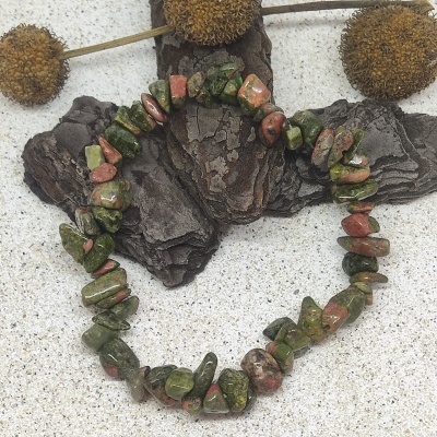 Pulseira de pedras verdes e vermelhas em fundo claro com casca de árvore e flores secas