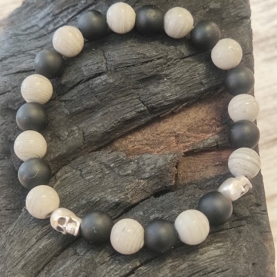 Pulseira de contas pretas e brancas com caveiras prateadas sobre madeira escura