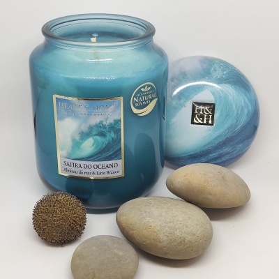 Vela azul em frasco de vidro com tampa azul decorativa e pedras lisas e semente marrom ao lado