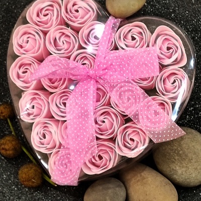 Caixa em forma de coração com rosas cor de rosa e laço rosa sobre pedras