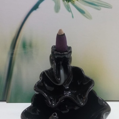 Incensário cerâmico preto com cone de incenso roxo e fundo de flor branca desfocada