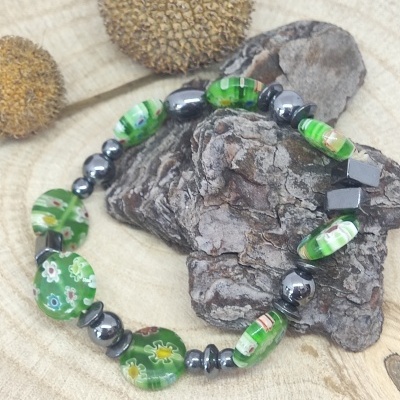 Pulseira verde com contas de vidro e metálicas sobre casca e madeira