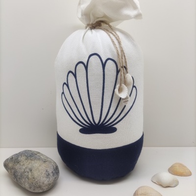 Saco tecido branco e azul com desenho de concha e cordão, conchas e pedra ao redor.