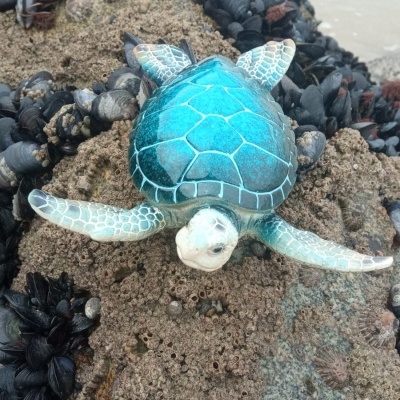 Figura decorativa de tartaruga azul sobre rocha com moluscos ao lado do mar