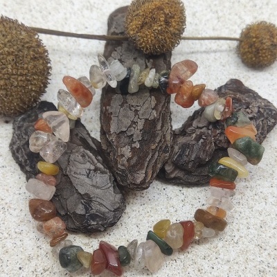 Bracelete de pedras semipreciosas multicoloridas sobre casca e fundo de areia com flores secas