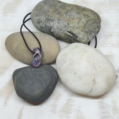 Colar com pendente de pedra roxa e cordão preto sobre pedras naturais coloridas