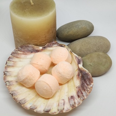 Sais de banho cor de pêssego em concha natural, vela bege e pedras lisas cinzentas