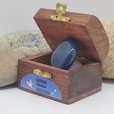 Caixa de madeira com pedra azul polida e etiqueta azul com texto e símbolo de Sagitário
