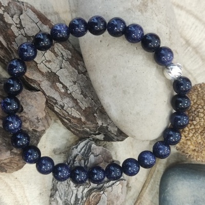Pulseira de contas azul-escuras com uma conta prateada sobre pedras e madeira