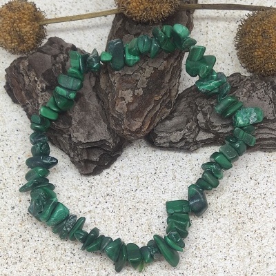 Pulseira verde de pedras irregulares sobre superfície clara com casca de árvore e flores secas