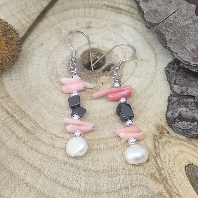 Brincos com pedras cor-de-rosa, negras e pérolas sobre madeira