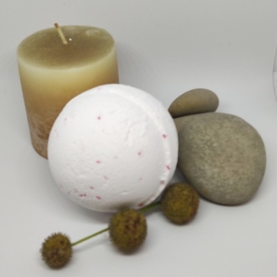 Vela creme, bomba de banho branca com pontos vermelhos, pedras cinzentas e flores secas sobre superfície branca