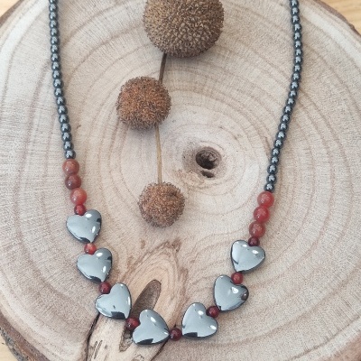 colar com contas prateadas, vermelhas e corações cinzentos sobre madeira rústica com frutos secos