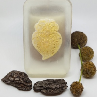 Sabonete transparente com detalhe amarelo em forma de flor, casca de árvore e flores secas ao lado