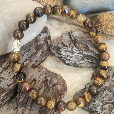 Pulseira de contas castanhas e dourada sobre cascas de madeira e pedras